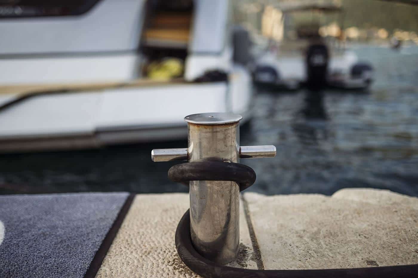 A metal cleat on a marina pontoon with a mooring rope tied to it