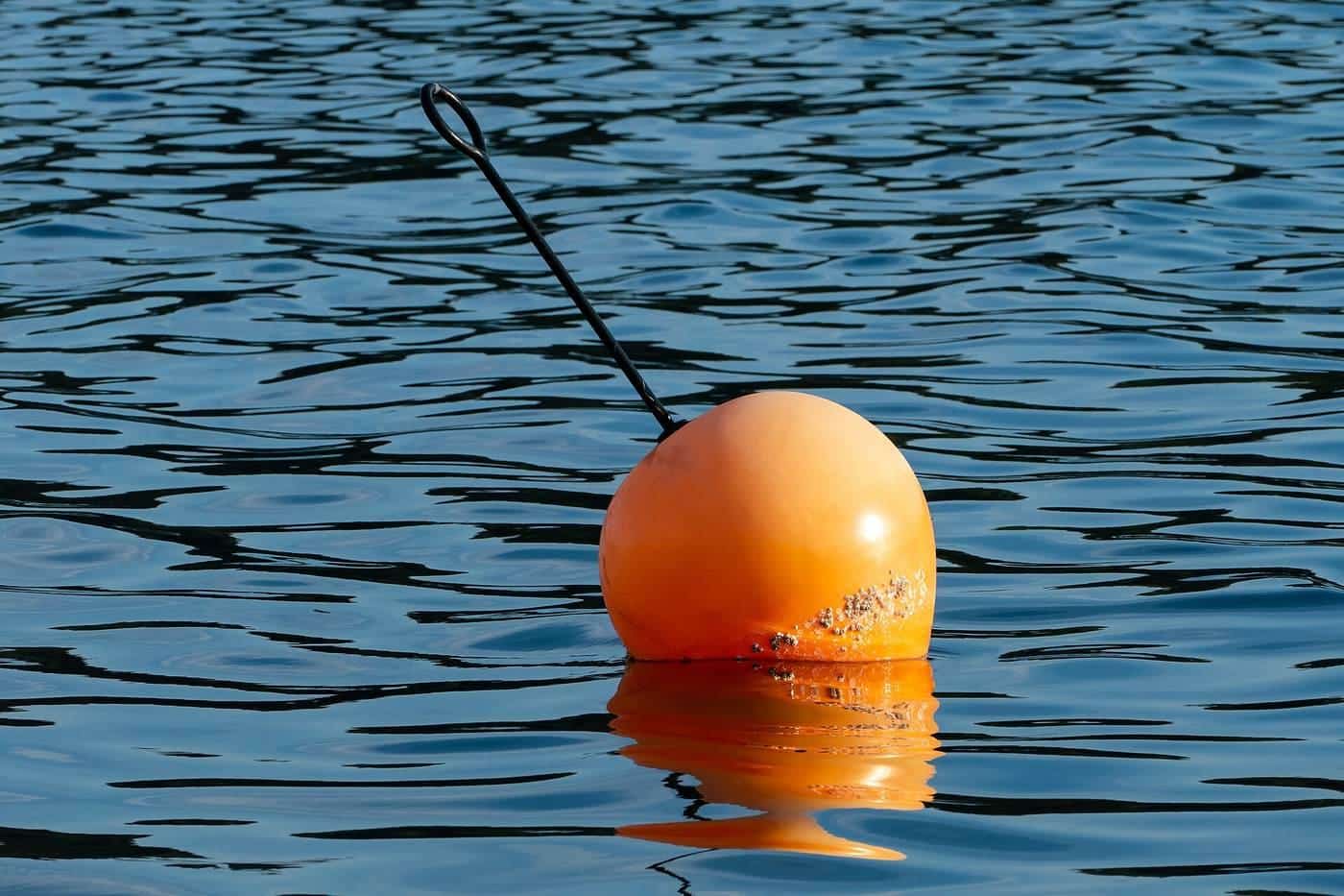 An orange mooring buoy with a pole floating on rippled blue water