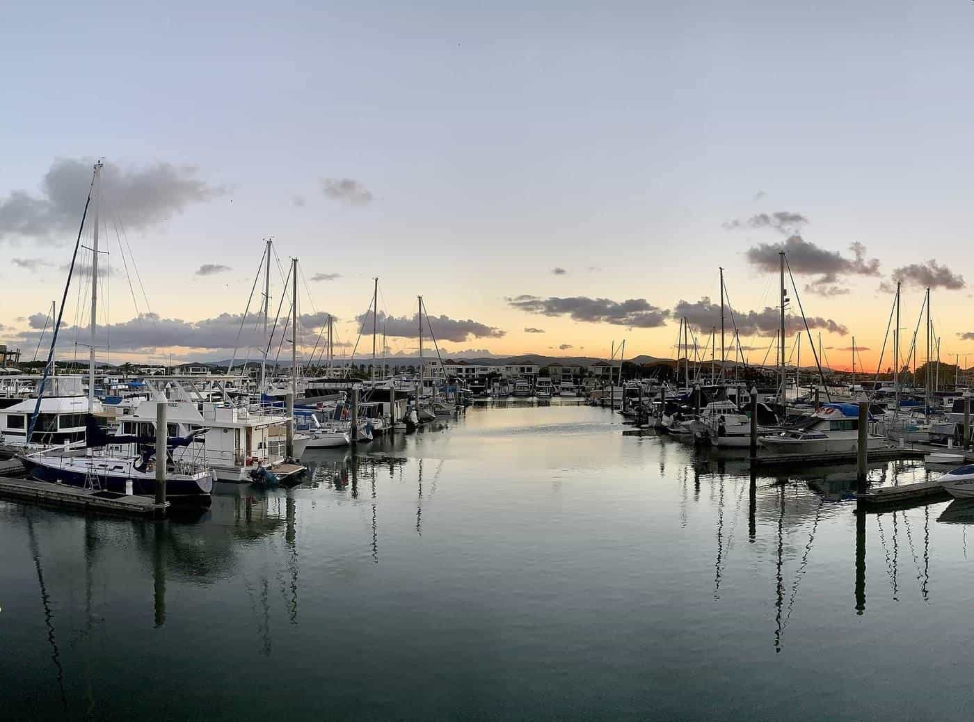 A calm marina at sunset with rows of yachts tied to pontoons