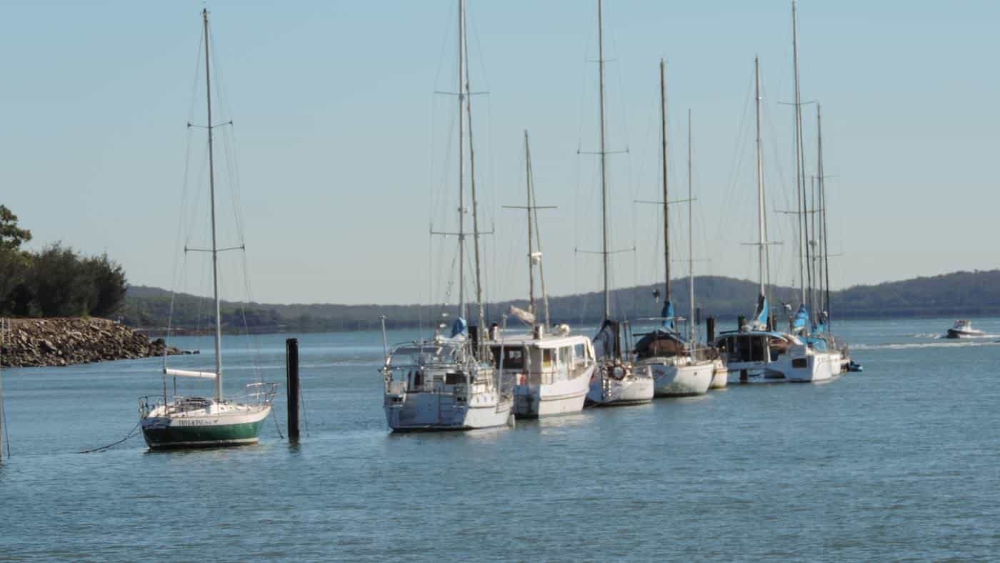 Yachts on moorings in a calm inlet with green hills behind