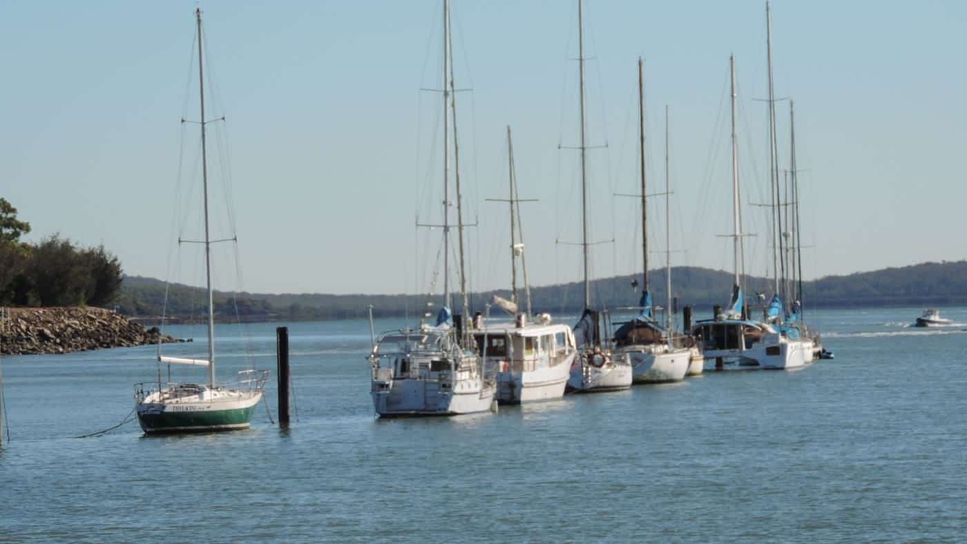 Yachts on moorings in a calm inlet with green hills behind