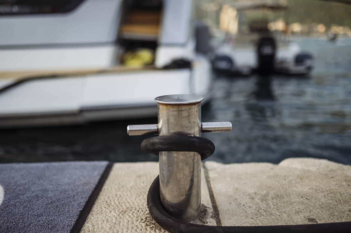 A metal cleat on a marina pontoon with a mooring rope tied to it