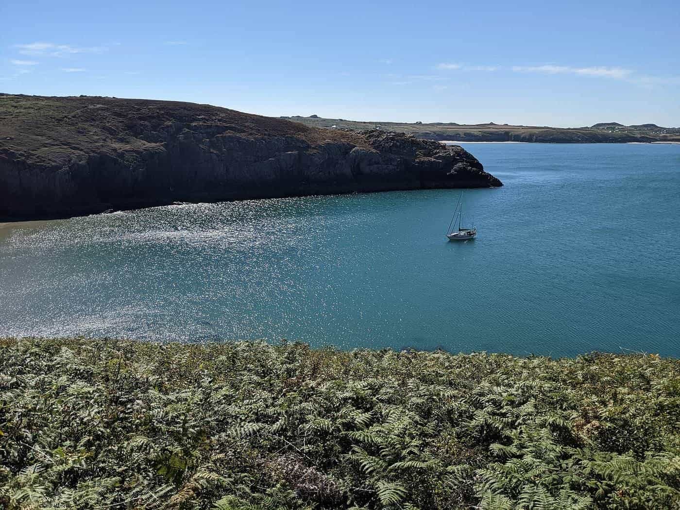 A single yacht anchored in a sheltered cove below a grassy headland